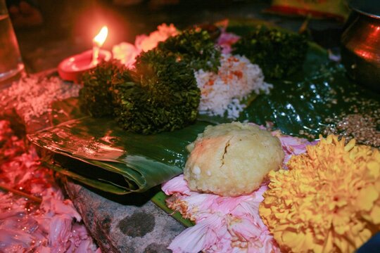 Banana leaf with ritual rice offerings and marigold flowers for Hindu ceremony, cultural traditions and ancestral worship with burning oil lamp in outdoor setting