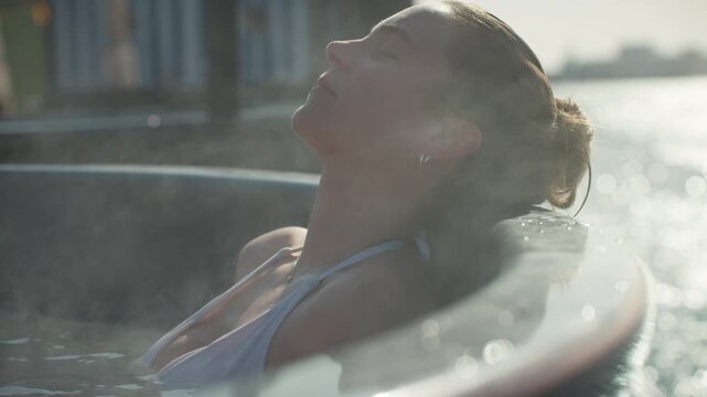 Spa calm surrounds the woman as she relaxes in a steaming hot tub by the water