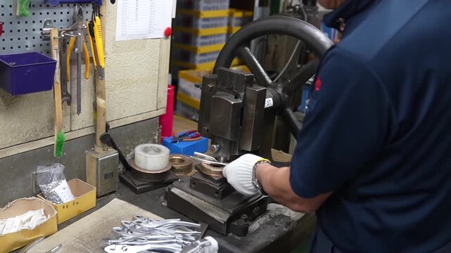 Worker at manual press station stamping brand markings onto small pliers handles with hand press