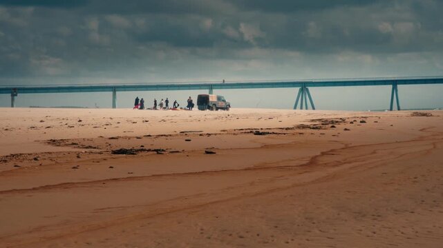 Wharf de la Salie structure towers over the beach with a van and people visible on the sand. Wide angle perspective showing the industrial architecture and sandy coast of Bassin d'Arcachon.