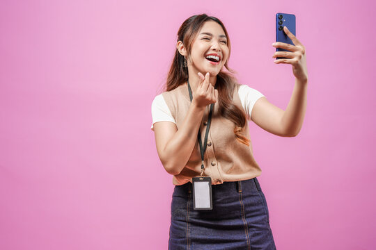 Lovely young Asian woman gesturing a finger heart while taking selfie with her smartphone.