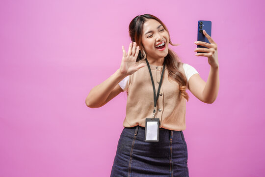 Smiling Asian woman in office attire is holding a smartphone and doing video call pose.