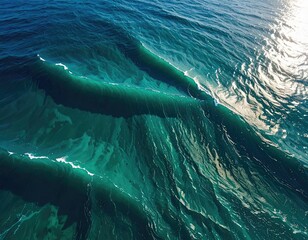 Naklejka premium Aerial view captures ocean waves with sun reflections. Teal and aqua colors create visual depth
