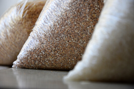 Plastic bags filled with various grains and groats on table close up