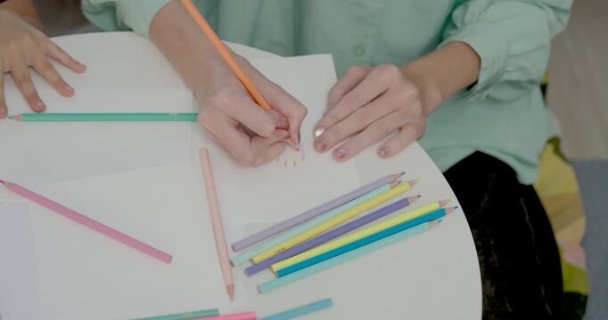Close view follows Caucasian mother drawing on paper with colored pencil while preschool daughter reaches in, turning home lesson into creative play, writing practice, and gentle guidance at home.