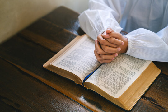 child hand clasped in prayer over the Holy Bible on a wooden table to pray and praise worship. praying to god. Christianity, spirituality, belief, religion, and faith with copy space.