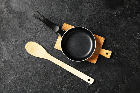 Empty frying pan and wooden spoon on cutting board, kitchen utensils for cooking and food preparation