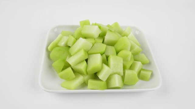 Handheld Shot of Diced Chayote on Rectangular Plate Isolated on White Background for Fresh Vegetable Preparation Concepts