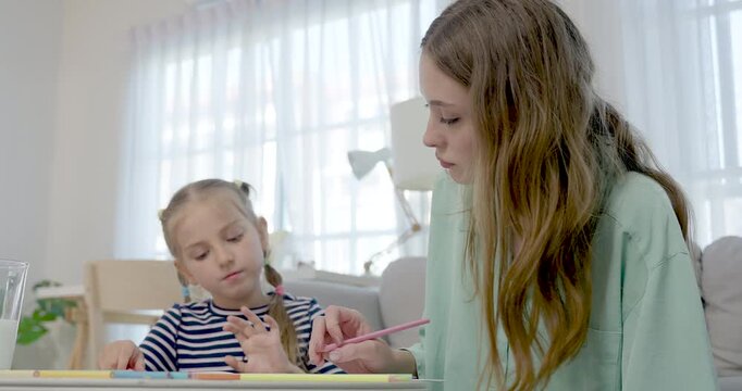 Caucasian single mother watches preschool daughter draw at cozy home table, passing colored pencil and giving calm guidance, building creativity, confidence, learning routine, parent child bond
