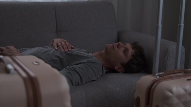 Relocation fatigue and homesickness. Young man lying on bed in temporary apartment feeling emotionally exhausted after moving