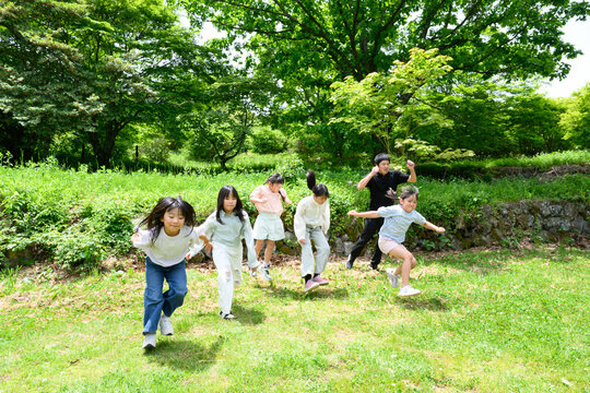 新緑の広場を元気よく走る複数人の小学生たち