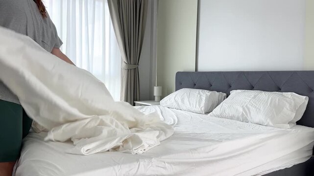 Home video footage of a woman putting a clean white duvet cover on a blanket in a bright bedroom, changing bedding as part of a housekeeping routine.