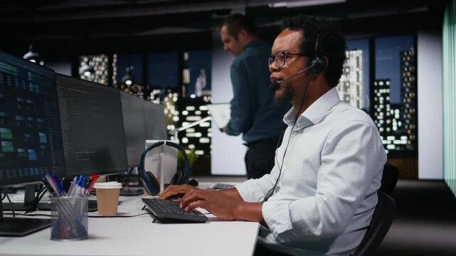 Startup helpdesk system administrator in office speaking in headset microphone, responding to service alerts with debugging context.