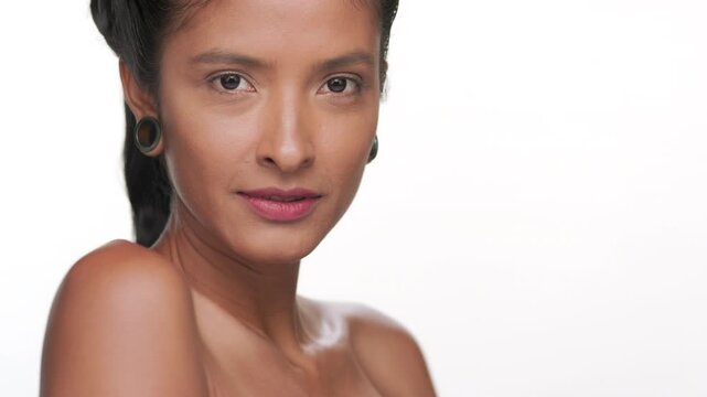 Close-up shot of latin woman with bronzed skin strokes her shoulder illustrating moisturized skin against white background | Face care commercial