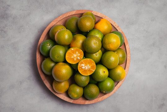 fresh mandarins piled on a wooden tray, featuring one sliced fruit revealing its juicy interio