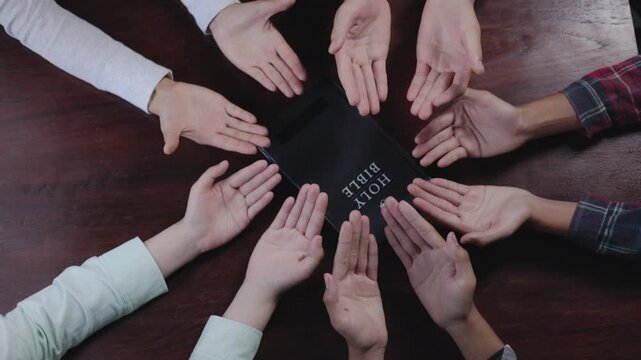 Group of Christian  holding hands praying worship together to believe and Bible on a wooden table for devotional for prayer meeting concept, teamwork.