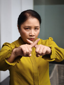 Middle aged asian woman asking to stop with rejecting x finger crossing gesture, staring at you
