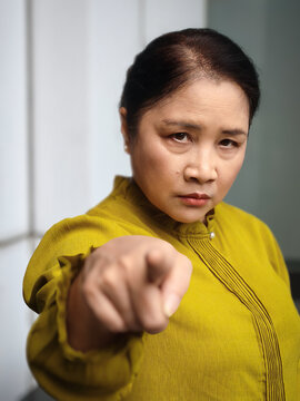Displeased, unhappy, upset, dissatisfied middle aged asian aunt woman with negative and hostile expression, pointing at you with angry mood