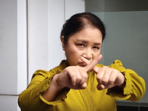 Middle aged asian woman asking to stop with rejecting x finger crossing gesture, staring at you