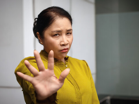 Middle aged asian woman asking to stop with stop hand sign gesture, staring at you