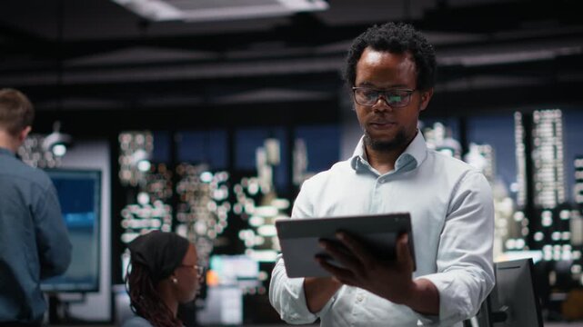 Engineer in office using tablet, working to fix bugs in AI system. IT worker troubleshooting neural network errors with device in tech agency workplace.