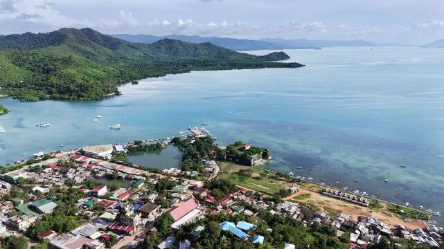 Push-in drone shot toward Fort Santa Isabel in Taytay, Palawan, revealing the coral-stone Spanish colonial fort nestled along the coastal town. The aerial glide highlights the tropical shoreline
