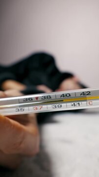 Close-up of a mercury thermometer shows a high fever, with a sick man lying down in the background. The camera focus shifts from the thermometer to the ill person on the floor.
