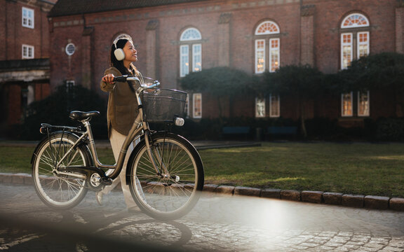 Woman with bicycle and headphones walking on campus