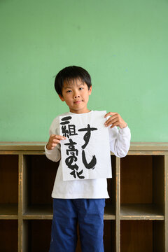 教室で自慢気に「すし」と書かれた習字の作品を見せる男子小学生