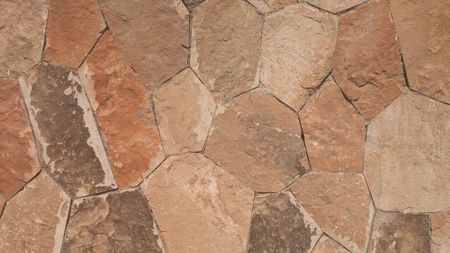 A close-up view of a natural stone wall with irregularly shaped tiles and earthy tones, showcasing a rustic texture and seamless pattern.