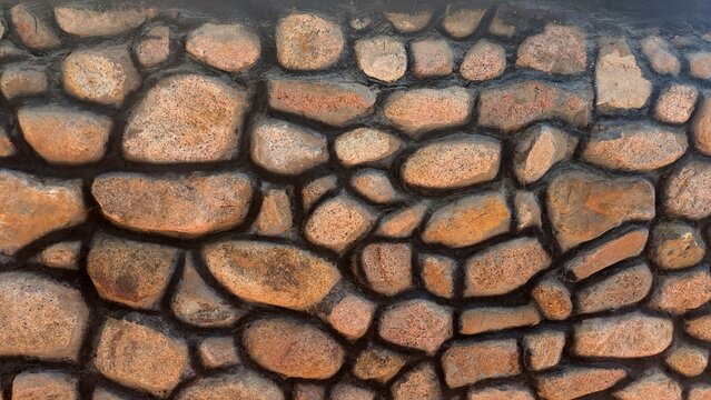A close-up view of a rustic stone wall with irregularly shaped stones and dark mortar, showcasing natural texture and earthy tones.