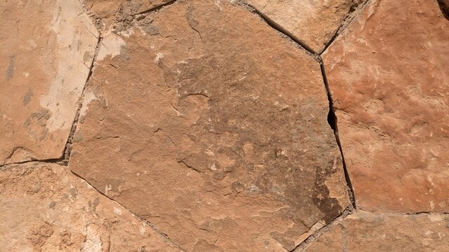 A close-up view of a weathered stone wall with natural textures and earthy tones, showcasing rugged stone surfaces and mortar joints.