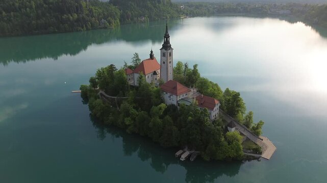 Aerial view of Bled Island with the Assumption of Mary Church on Lake Bled, Slovenia. Beautiful cinematic footage of the iconic island surrounded by turquoise blue water and Alps mountains