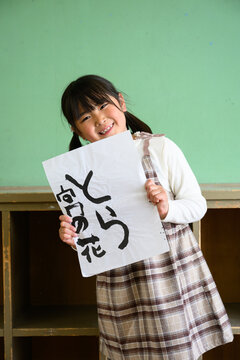 教室の後ろで笑顔で「とら」の習字作品を高く掲げる女子小学生	