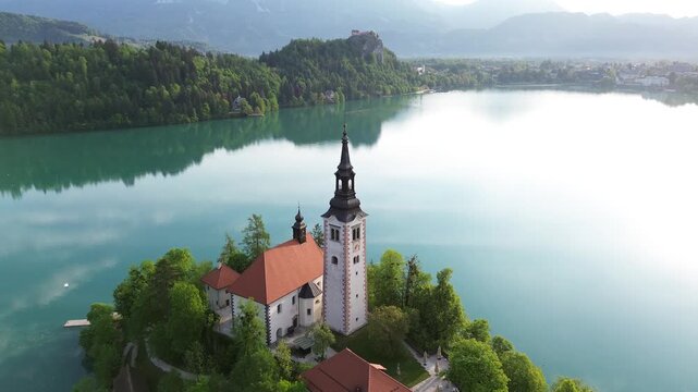 Aerial view of Bled Island with the Assumption of Mary Church on Lake Bled, Slovenia. Beautiful cinematic drone footage of the iconic island surrounded by turquoise blue water and Alps.