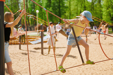 Girl having fun on a rope climbing frame at a playground on a sunny day. Summer activity. Childhood. © khmelev