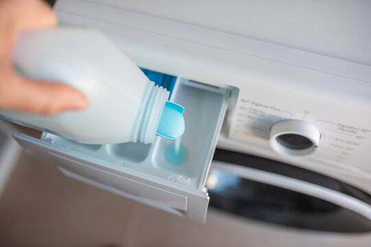 Hand of white European woman pouring liquid detergent into washing machine
