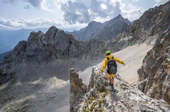 Hiker balancing on rocky outcrop, hiking trail to Lamsenspitze, in the background cirque and rocky mountain peak with Mitterkarlspitze, Karwendel Mountains, Alpenpark Karwendel, Tyrol, Austria