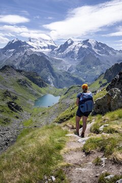 Hiker on hiking trail, mountain lake Lac de Louvie with glaciated summit of the Grand Combin, Val de Bagnes, Valais, Switzerland