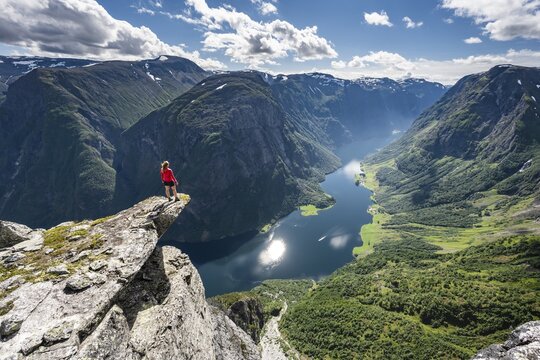 Hiker standing on rocky outcrop, view from the top of Breiskrednosi, mountains and fjord, N&aelig;r&oslash;yfjord, Aurland, Norway
