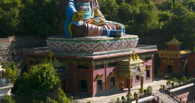 Drone moves from a lower angle upward while orbiting around the colorful Guru Rinpoche statue, showing the green hillside landscape in Pharping, Nepal, and lush mountain environment in the background