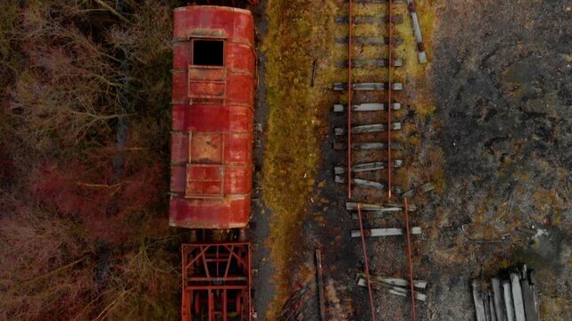 Birds-eye drone footage looking straight down onto derelict, heavily rusted red train carriages sitting on decaying narrow-gauge tracks at the historic Dunaskin industrial heritage site in Ayrshire