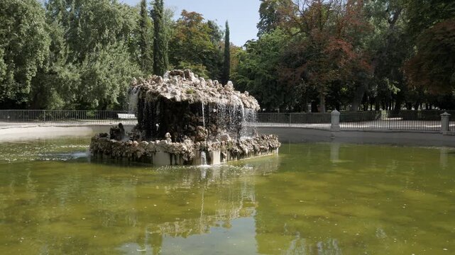 Stone fountain with cascading water in a quiet park surrounded by green trees