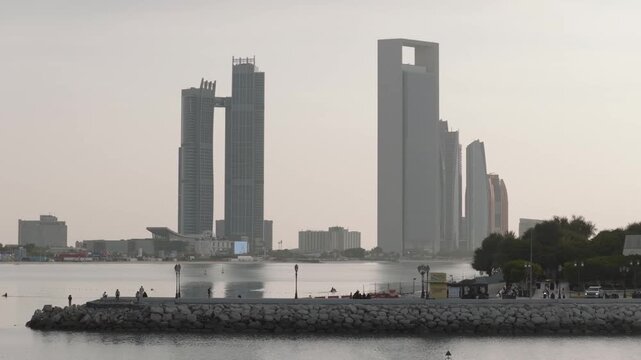 Drone tracks right past a traditional dome building, panning slightly to keep the modern Abu Dhabi skyscraper skyline centered on the horizon.