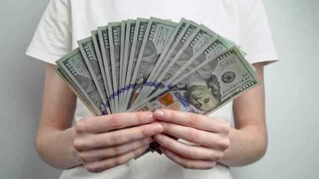 Woman in white t-shirt counting stack of dollar banknotes. Personal finance, cash savings, income, wealth, investment, budgeting and money management concept.