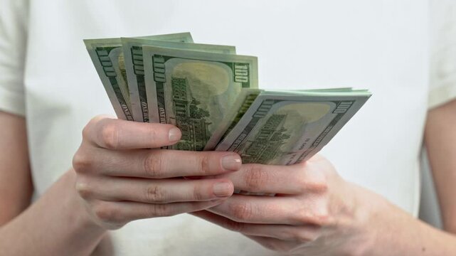 Woman in white t-shirt counting stack of dollar banknotes. Personal finance, cash savings, income, wealth, investment, budgeting and money management concept.