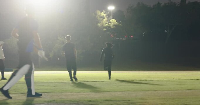 Male team bowler running batsman swinging keeper catching fielder returning under lights