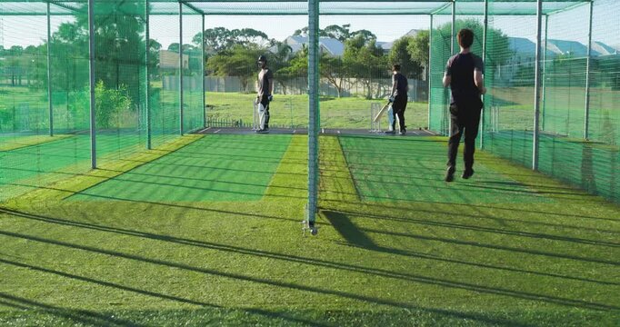 Male teammates switching at nets batting and bowling, batsman adopting stance for drill