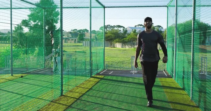 Cricket teammates inspecting turf, moving stumps, bowling ball toward target in practice net