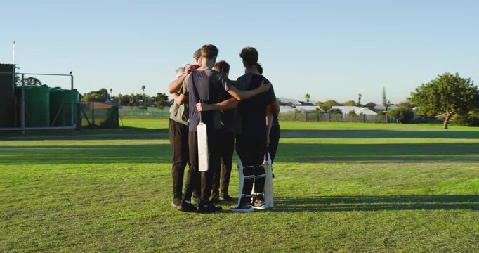 Teen male teammates huddling on outfield cheering to boost spirit, walking to pitch with bats